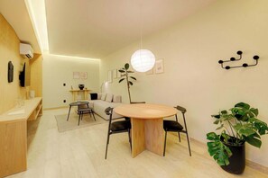 Un espace repas moderne avec une table ronde en bois, des chaises noires, une plante en pot et un luminaire suspendu.