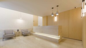 Zona de recepción con mostrador, dos sillones, una mesita con un florero e iluminación colgante.