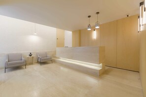 A reception area with a reception desk, two armchairs, a small table with a vase, and pendant lighting.