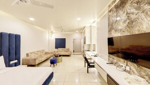 Una habitación de hotel moderna con una cama grande, dos sofás, un televisor y un minibar.