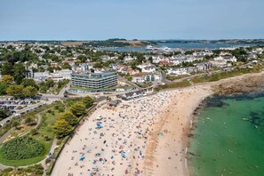 An aerial view of a coastal town with a sandy beach, a modern building complex, and residential houses.