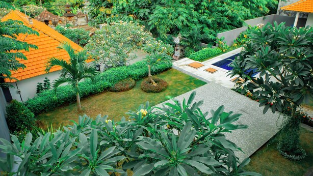 Un cortile con piscina, circondato da vegetazione lussureggiante e un edificio tradizionale con tetto in tegole.