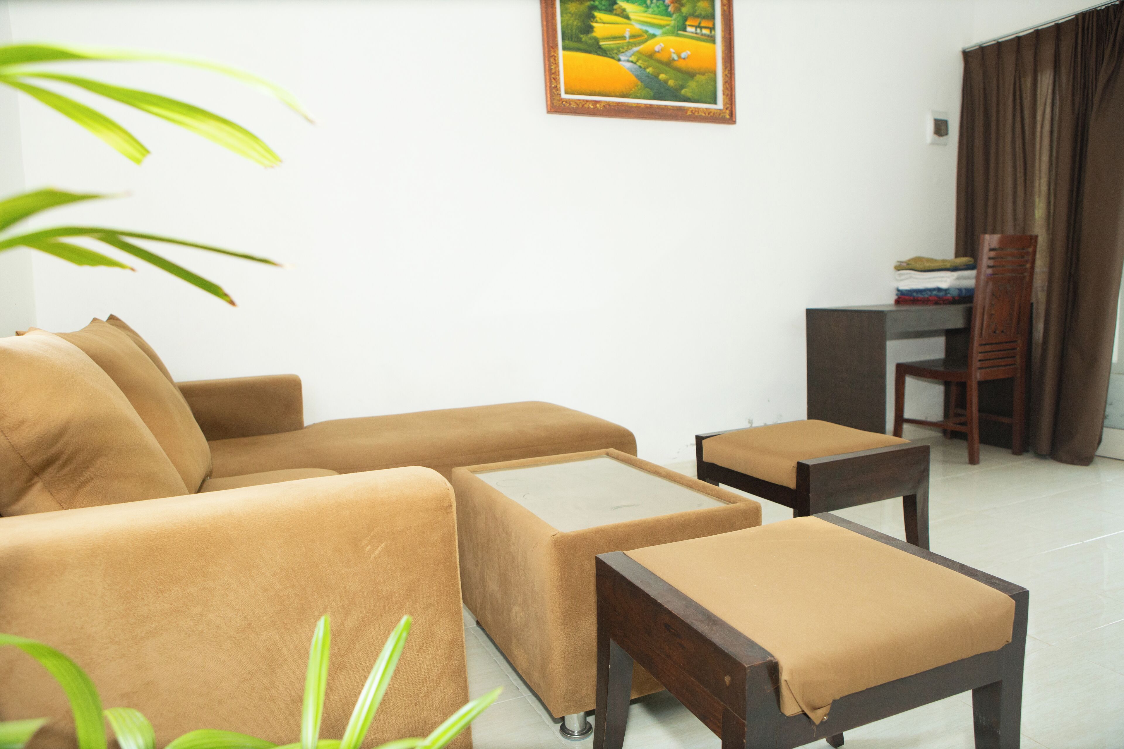 A living room with a sofa, a coffee table, and a chair. There is a painting on the wall and a plant in the corner.
