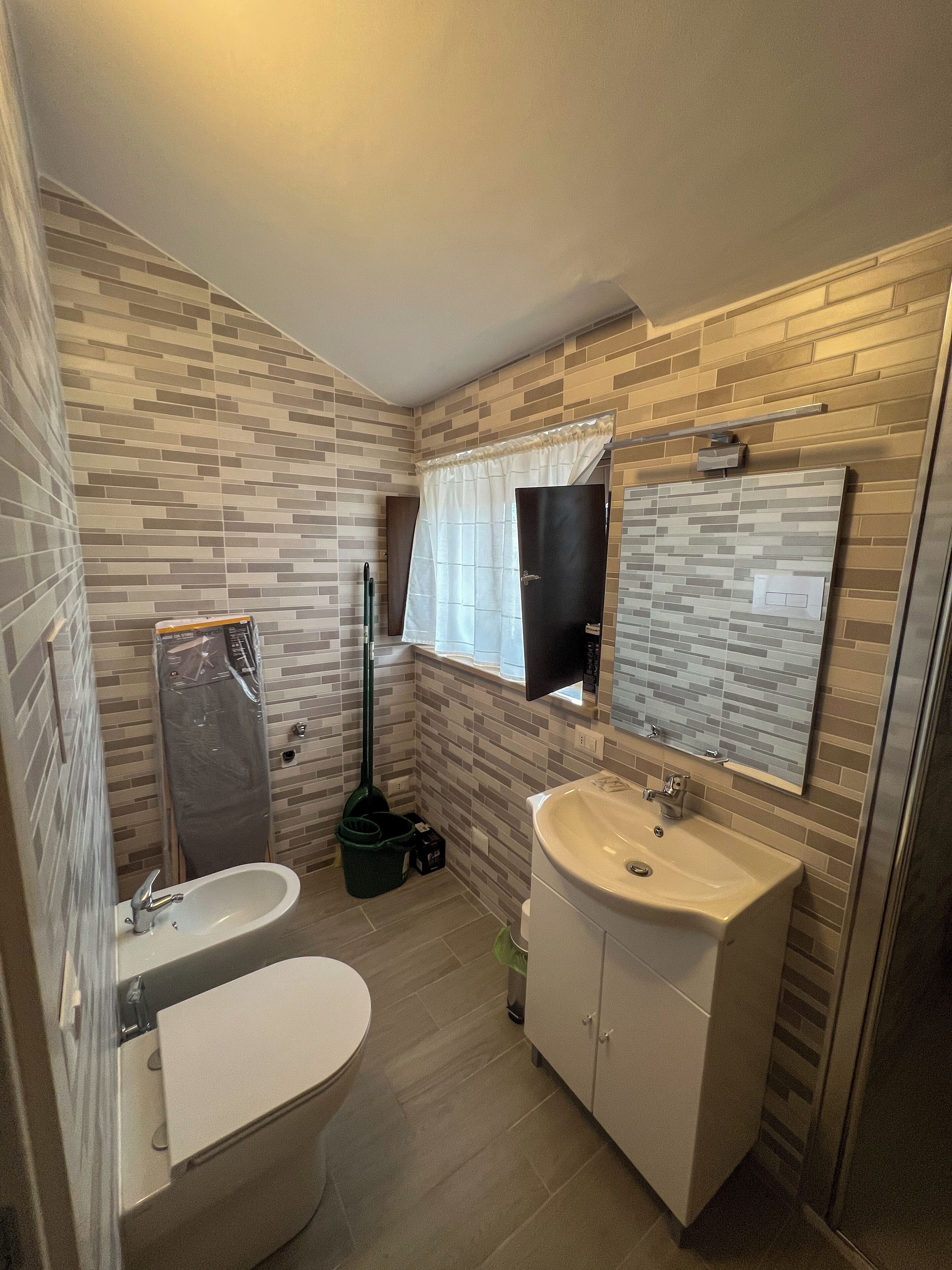 Un baño con salpicadero de azulejos, un inodoro, un lavamanos y un espejo.