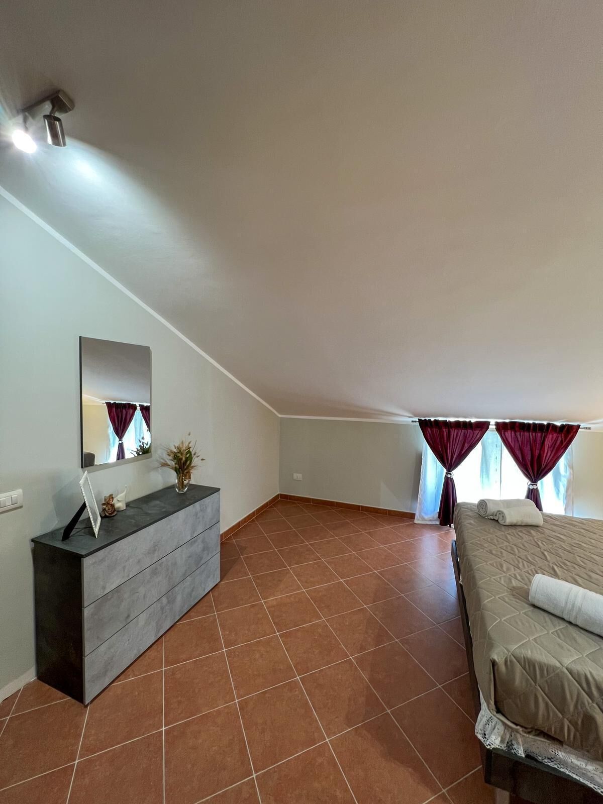 Una camera da letto con un letto, una cassettiera, uno specchio e una finestra con tende.