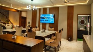 A modern dining area with a large TV screen, wooden paneling, and a ceiling fan. - The Infinity Villa (Madikeri)