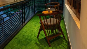A balcony with a table and chairs, surrounded by large windows offering a view of trees and buildings. - The Infinity Villa (Madikeri)