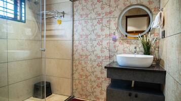 A bathroom with a glass shower enclosure, a white sink with a mirror above it, and floral-patterned tiles.