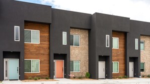 A modern multi-story residential building with a dark facade, wooden panel accents, and uniform door designs. - HowdyHouse: Designer Townhouse in Historic FOODIE  Bryan Minutes to Kyle Field (Bryan)