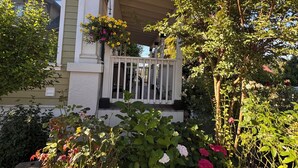 A house with a porch, a garden with various plants and flowers, and a clear blue sky. - Located near wineries, tulip festival, outlets, Bauman’s Fram & state parks! (Mount Angel)