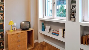 Ein Zimmer mit einem Holzkasten, einem Fernseher und einem Fenster mit Regalen darüber.
