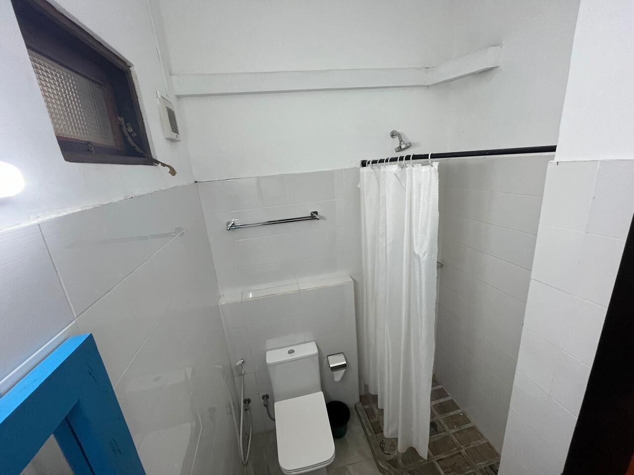 Casa de banho pequena e compacta com azulejos brancos, sanita, zona de duche e espelho com moldura azul.