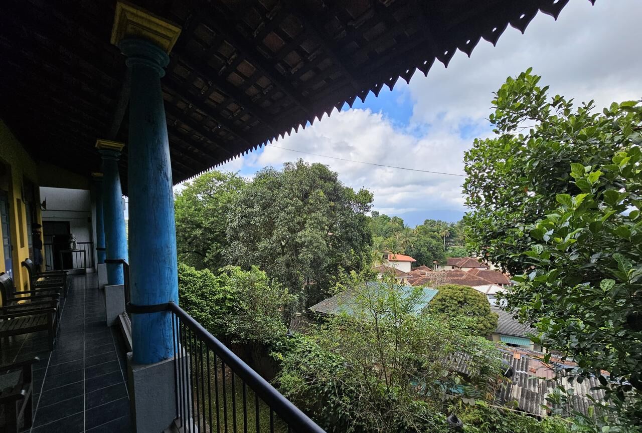 A covered balcony with blue columns, a tiled floor, and a view of a residential area with trees and houses.