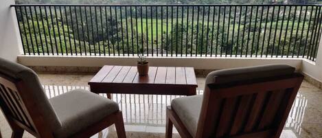 A balcony with two wooden chairs and a table, overlooking a lush green landscape.