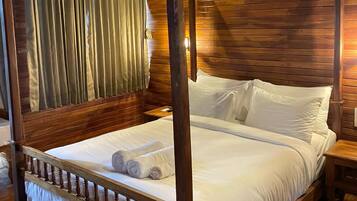 Uma cama de dossel com lençóis brancos e estrutura de madeira, um ventilador de teto e lambris de madeira nas paredes.