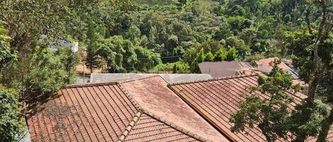 A view of a residential area with terracotta-tiled roofs, surrounded by lush greenery and hills in the background.
