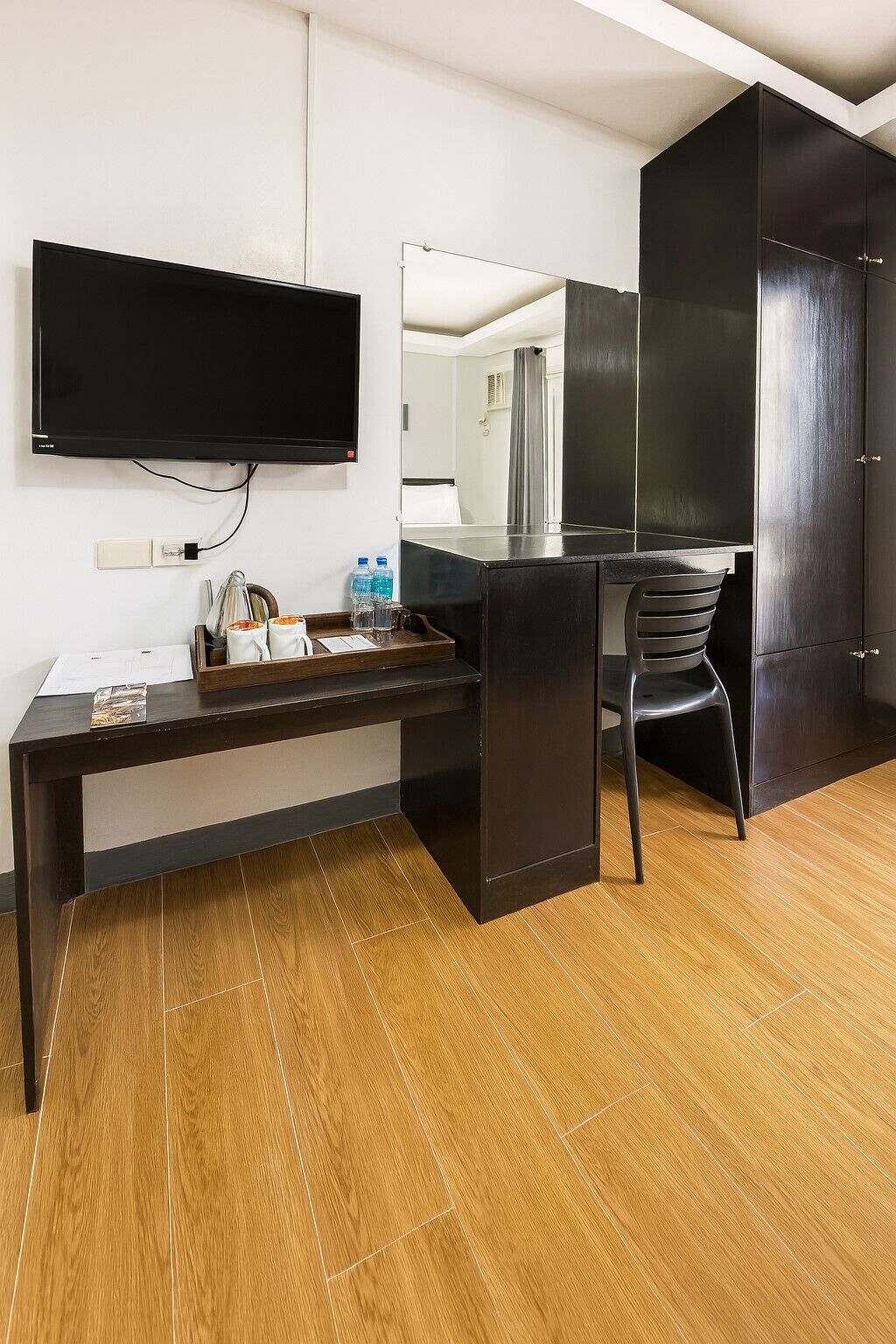 Habitación de hotel moderna con un escritorio de madera oscura, un televisor de pantalla plana en la pared y un espejo grande.