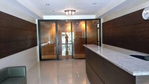 Un área de recepción moderna con puerta de entrada de vidrio, mostrador de recepción y un reloj en la pared.