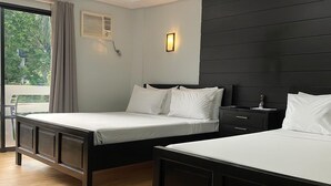 Habitación de hotel con dos camas, un ventanal con cortinas, aire acondicionado instalado en la pared y una mesita de noche con lámpara.
