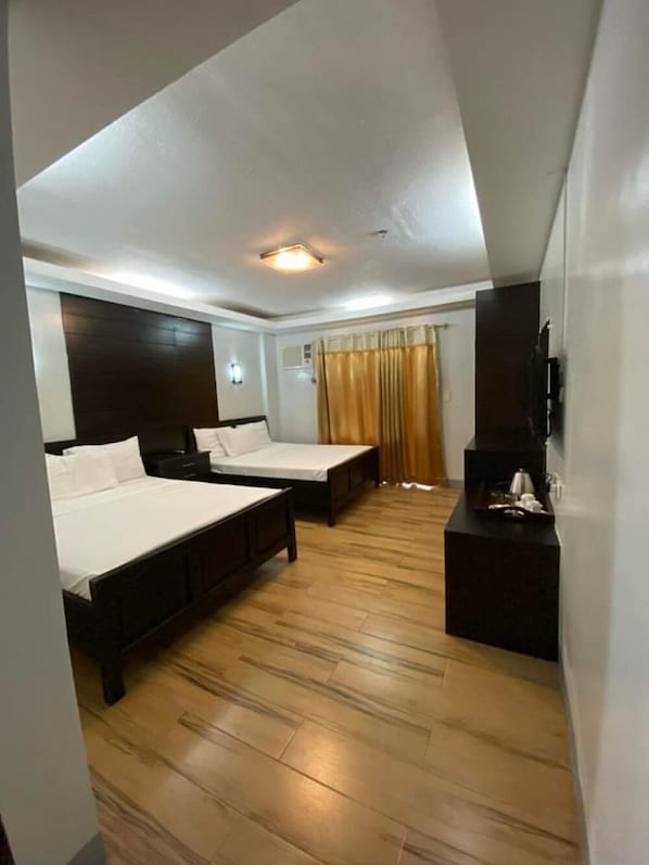 Habitación de hotel con dos camas, un televisor de pantalla plana, una mesita de noche y una ventana con cortinas.