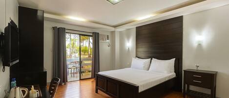 Quarto de hotel com cama, mesa de cabeceira, televisão e escrivaninha com cadeira.