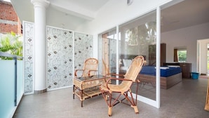 A spacious balcony with wicker furniture, a glass door leading to a bedroom, and a patterned wall.