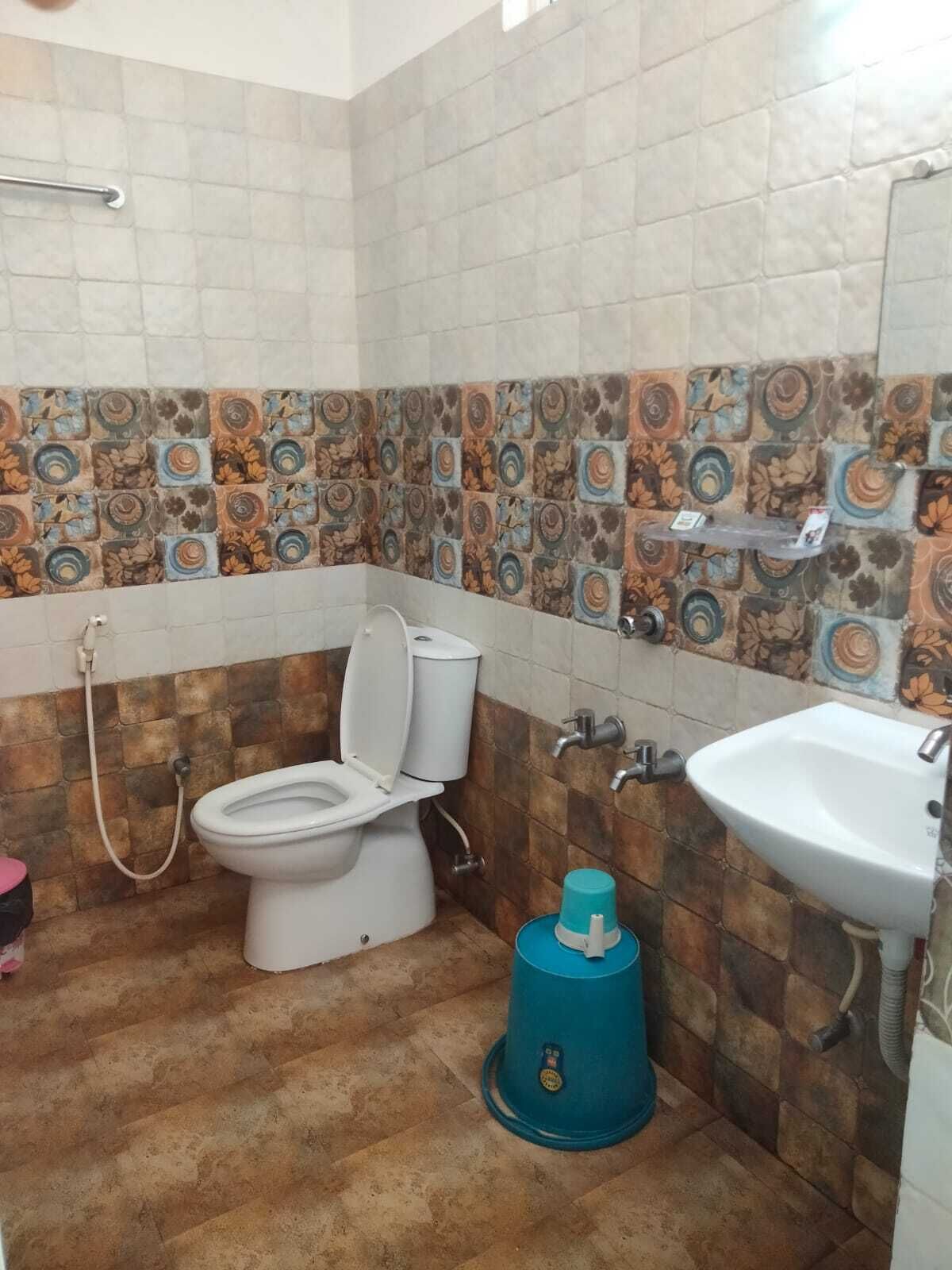 A bathroom with a toilet, sink, and a blue cleaning bucket.