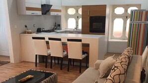 Et moderne køkken med en central ø, spisebordsstole, en sofa med mønstrede puder og en stribet gardin.