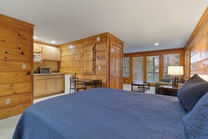 A log cabin-style bedroom with a large bed, wooden walls, a kitchenette, and a view through the windows. - Golfing Dreams (Pigeon Forge)