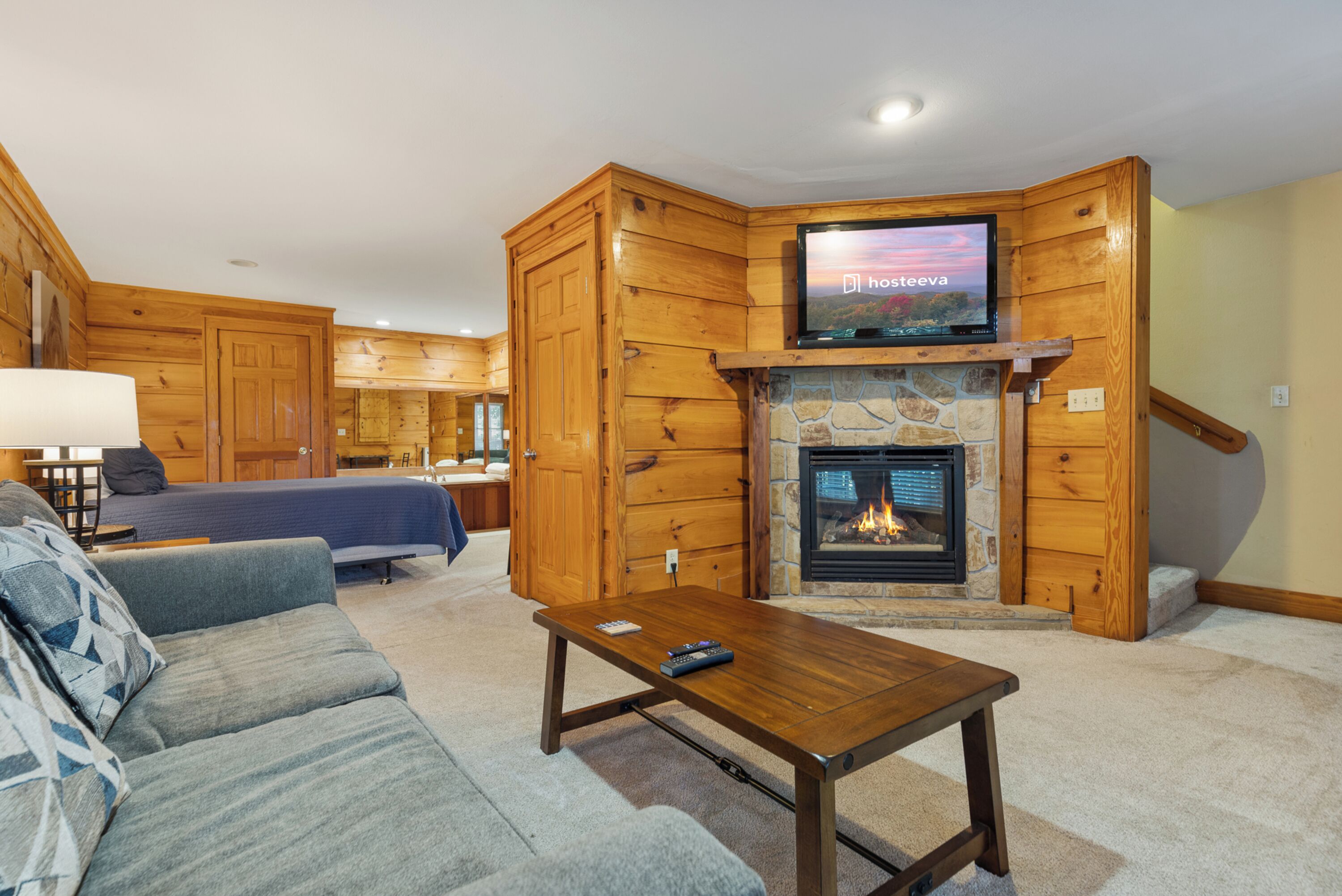 Un salón acogedor con chimenea de piedra, paredes de madera, televisor de pantalla plana y un sofá cómodo.