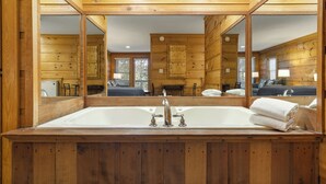 Interior de una cabaña de madera con una bañera grande, paredes de madera y un espejo que refleja la habitación.