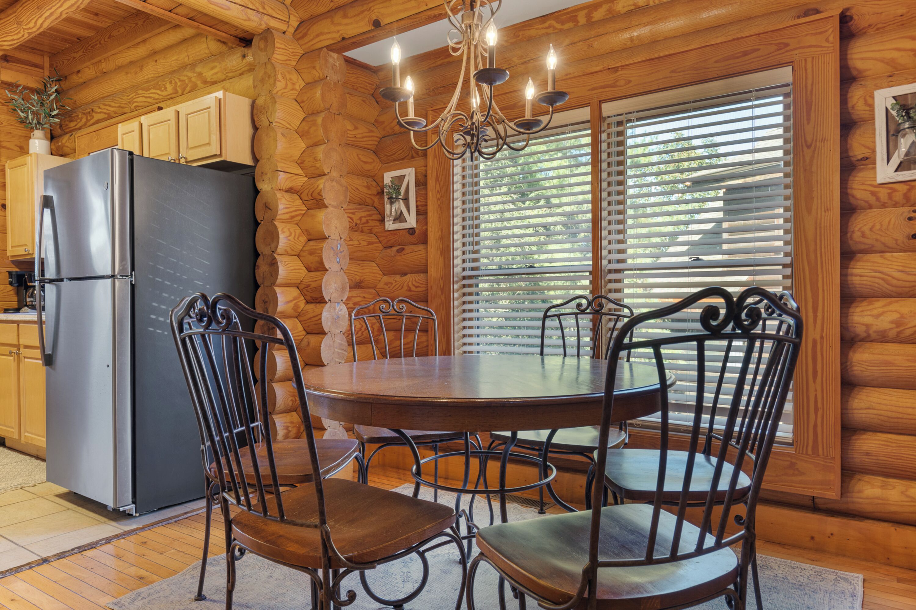 A wooden cabin interior with a dining table, chairs, a refrigerator, and a chandelier.