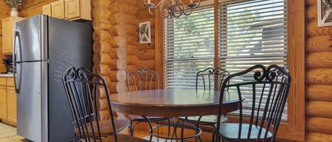 A wooden cabin interior with a dining table, chairs, a refrigerator, and a chandelier.