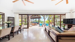 Amplia sala de estar con puerta de vidrio que da a una piscina, un conjunto de sofás, una mesa de comedor y un televisor.