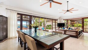 Amplia sala de estar con mesa de comedor de vidrio, asientos cómodos, televisión y ventilador de techo.