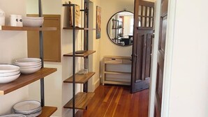 A hallway with wooden flooring, shelves with bowls, a mirror, and a door with a light fixture. - Quissett Landing | Sleeps 12 | Walk to The Knob (Falmouth)