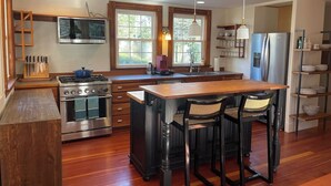 A kitchen with a central island, a stove, and bar stools. - Quissett Landing | Sleeps 12 | Walk to The Knob (Falmouth)