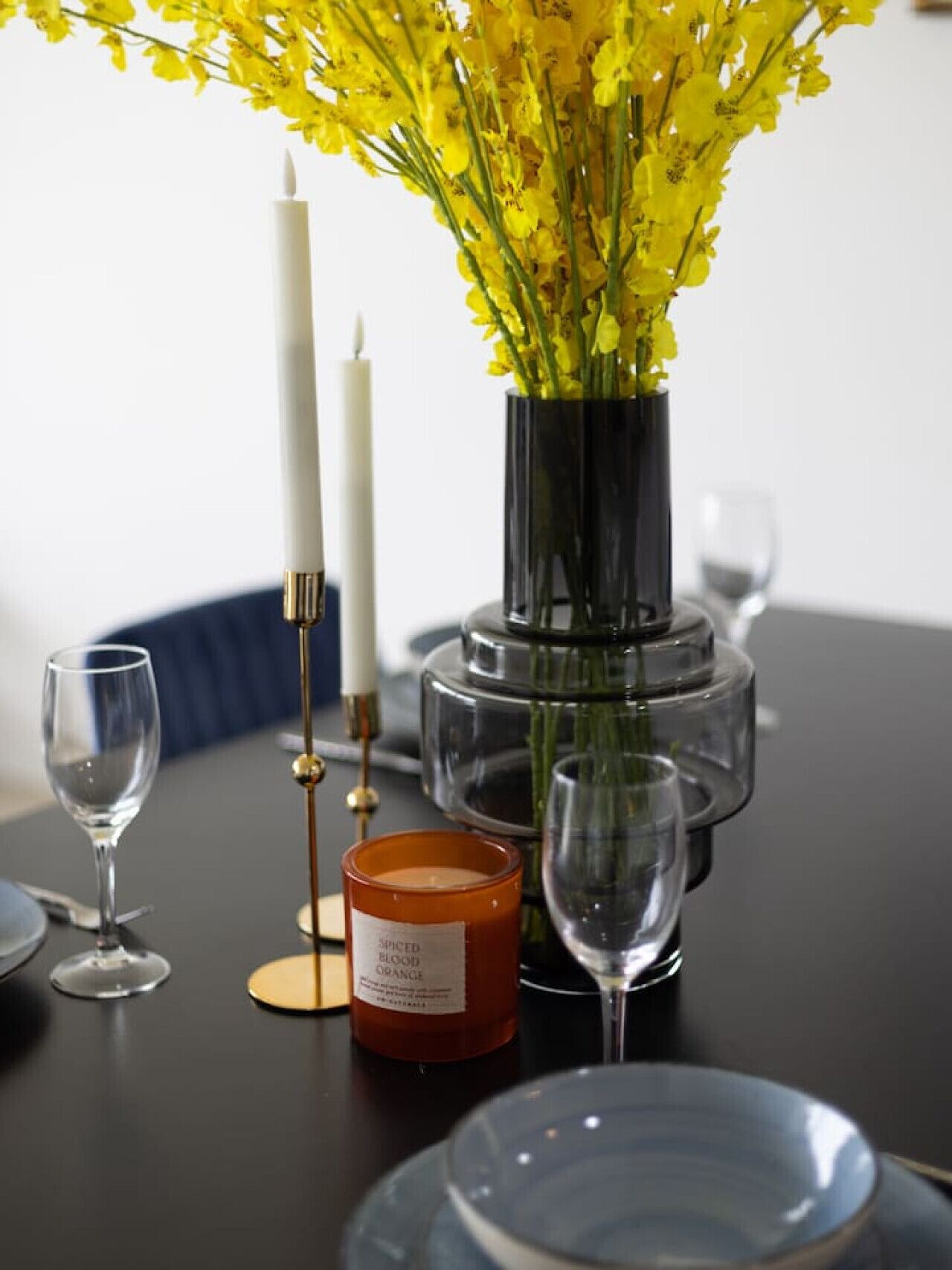 Et spisebord med en vase med gule blomster, stearinlys og et stearinlys mærket "SPICED BLOOD ORANGE".