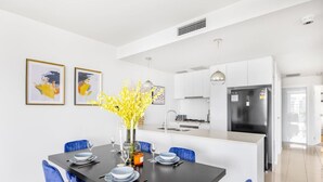 A modern kitchen with white cabinets, a black refrigerator, and a dining area with a black table and blue chairs.