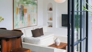 Una sala de estar moderna con un sofá blanco, una mesa de centro de madera, un ventilador de techo y un cuadro abstracto de gran tamaño.