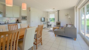 A modern kitchen with white cabinets, a dining table with chairs, a grey sofa, and a TV in the living area.