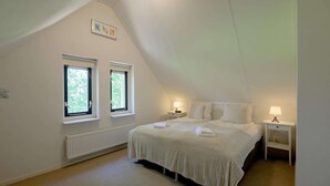 A bedroom with a sloped ceiling, two windows, a bed with white bedding, two bedside tables with lamps, and a radiator.