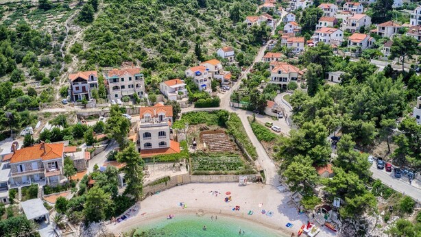 Eine Vogelperspektive auf ein Küstendorf mit terrassenförmig angelegten Häusern, einem Strand und klarem türkisblauem Wasser.