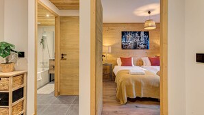 Un dormitorio con techo de madera, una cama con manta blanca y naranja, un cuadro de ciervos y una lámpara colgante.