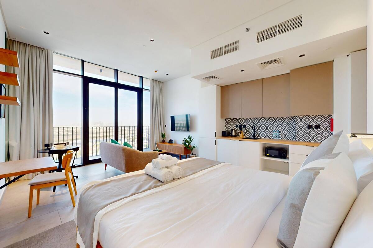Une chambre d’hôtel dotée d’un grand lit, d’un bureau, d’une chaise, d’un balcon avec vue, d’une kitchenette et d’une télévision.