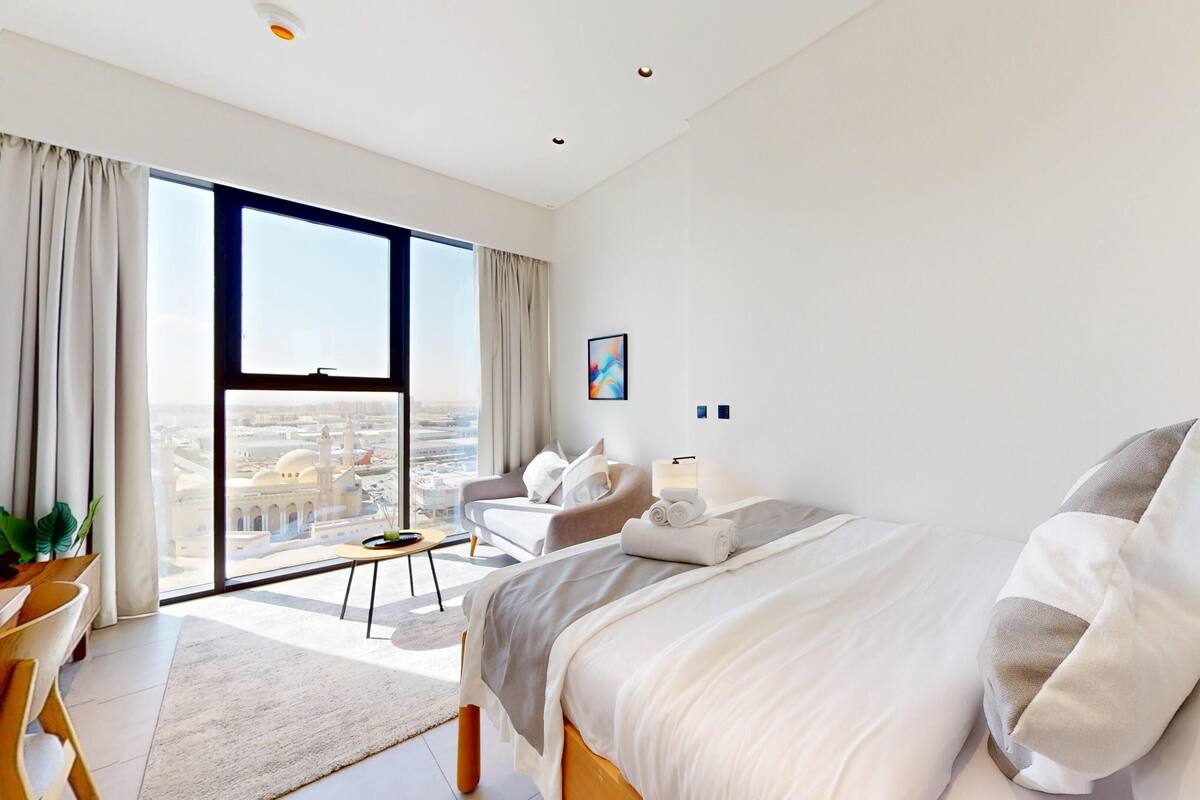 Une chambre d’hôtel moderne avec une grande fenêtre, un lit, une chaise et une petite table.