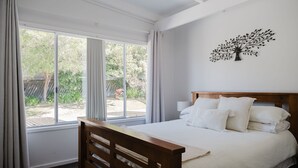 Ein Schlafzimmer mit großem Fenster, einem Bett mit weißer Bettwäsche und einem an der Wand befestigten Baumdekor.