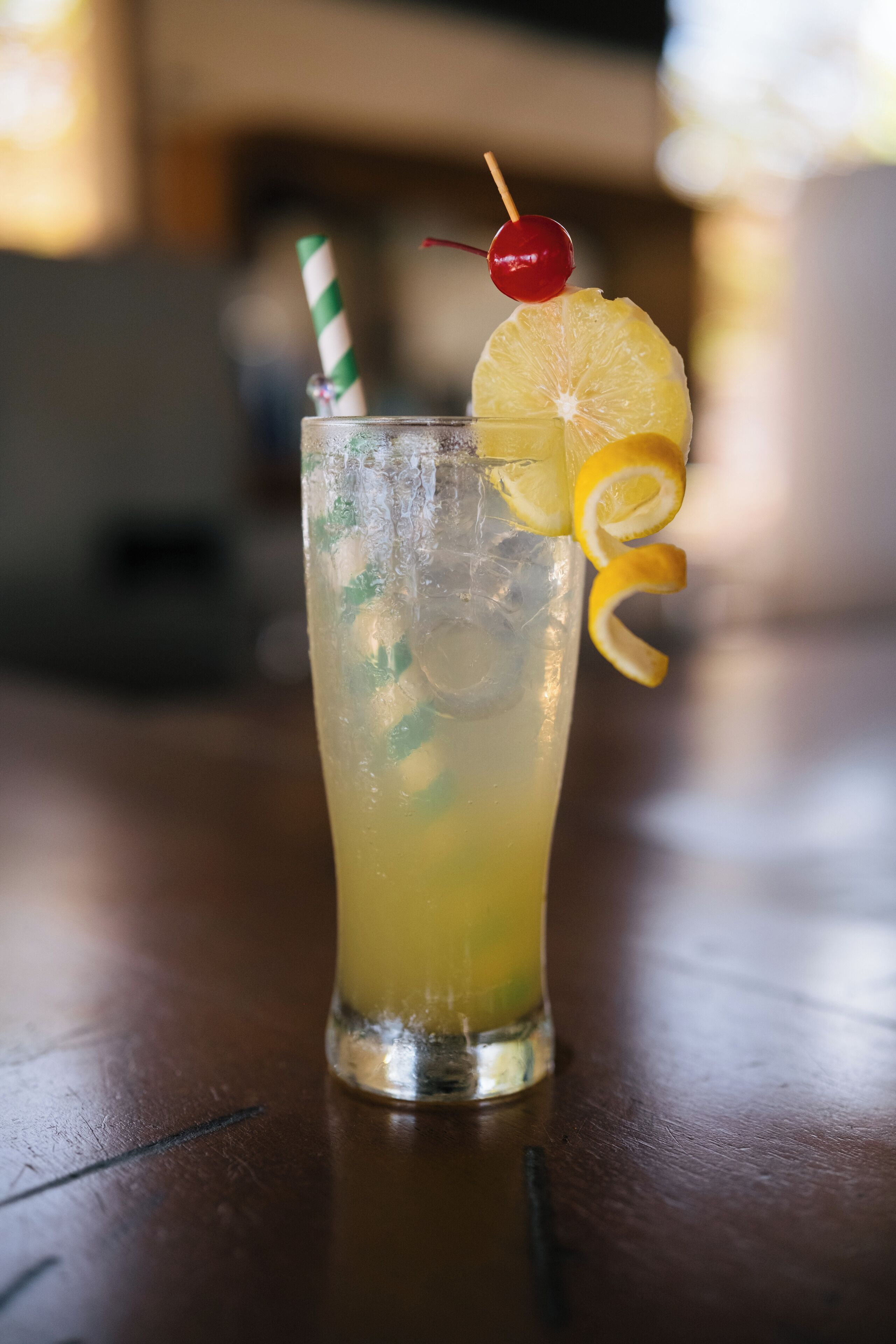 Un grand verre contenant une tranche de citron, une cerise et une paille rayée.