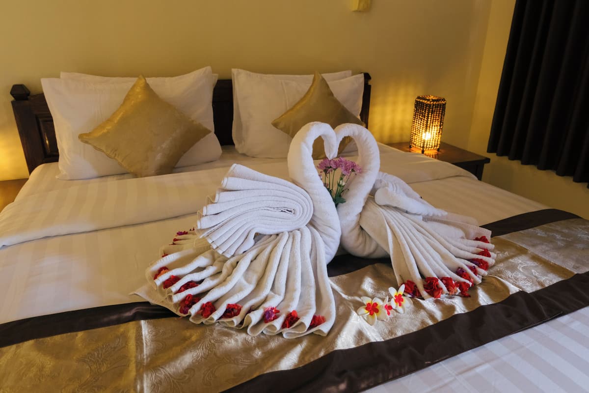A neatly made bed with white linens and a decorative swan towel arrangement.