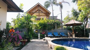 A pool area with lounge chairs, a small table, and a decorative umbrella. - New Starlight Hotel & Resort (Buleleng)